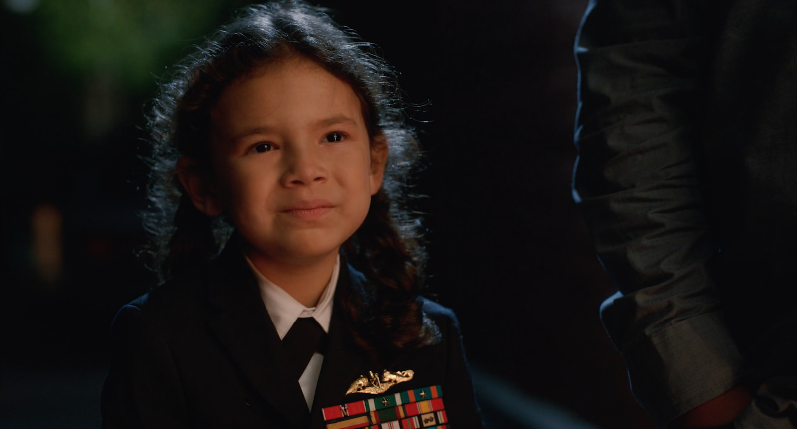 a little girl in a uniform standing next to a man