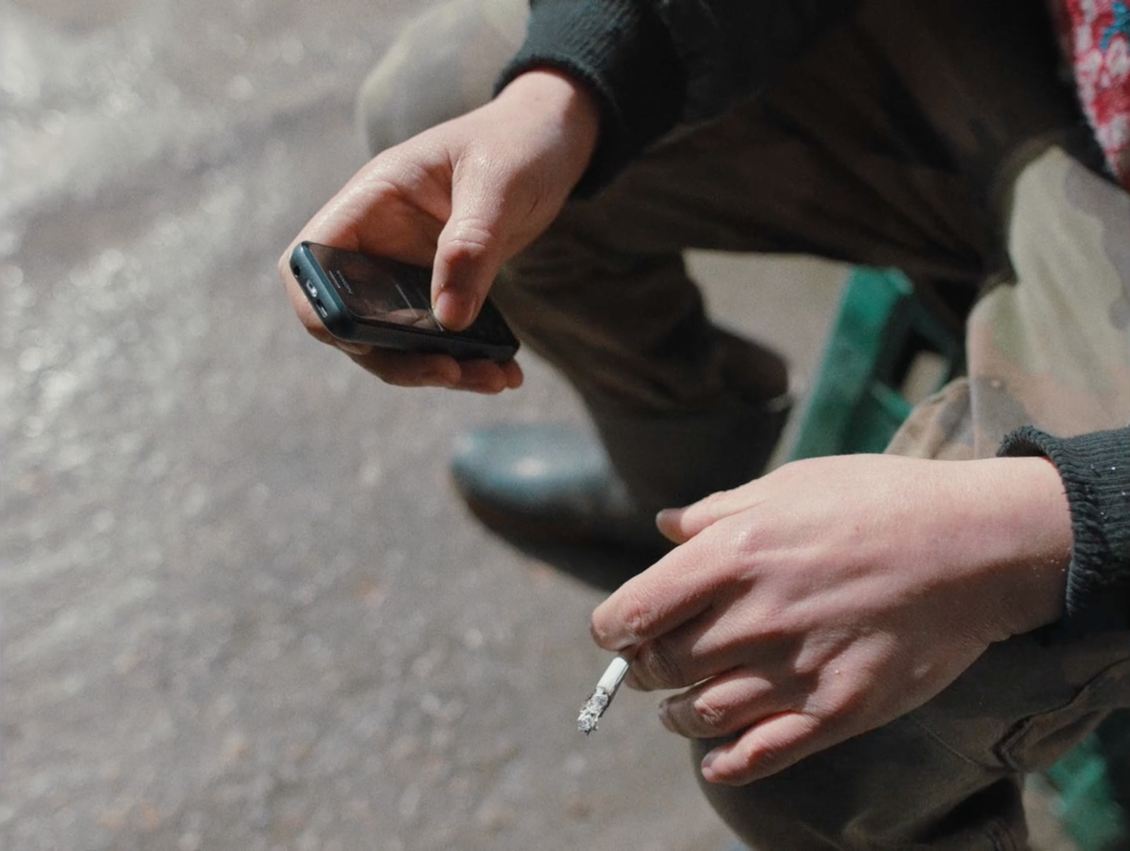 a person sitting on a bench holding a cigarette and a cell phone