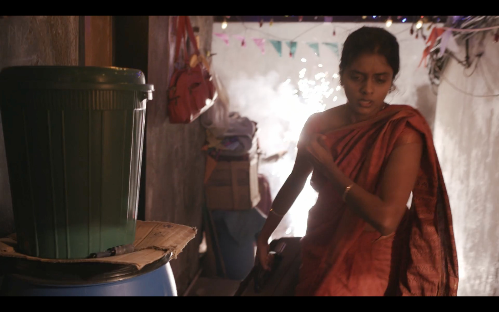 a woman in a red sari is standing in a room with a trash can