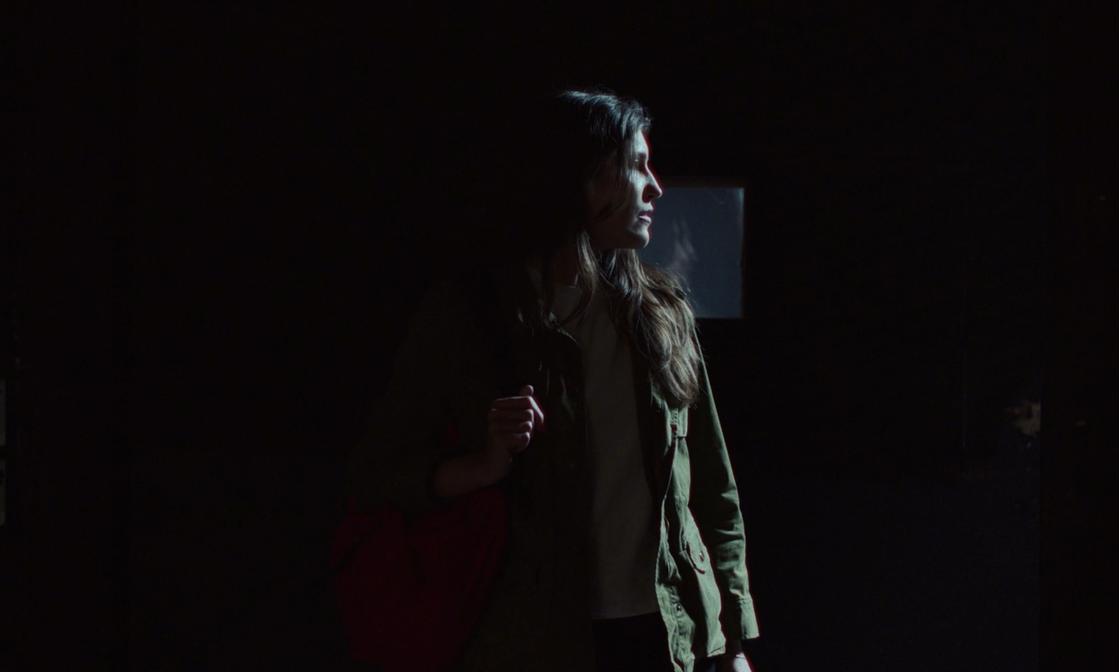 a man standing in the dark holding a red bag