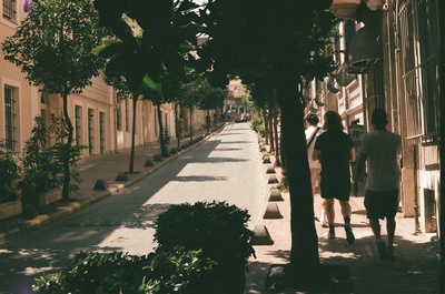 a couple of people walking down a street next to tall buildings