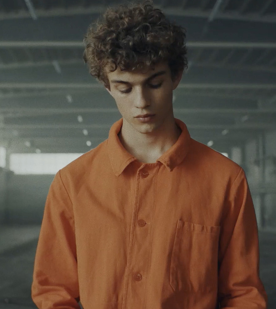 a man in an orange shirt looking down at his cell phone