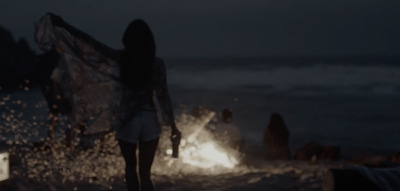 a woman standing on a beach next to a fire