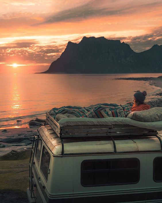 a person laying on top of a van next to a body of water