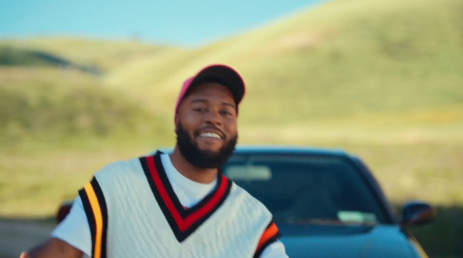 a man with a beard and a baseball cap smiles in front of a truck