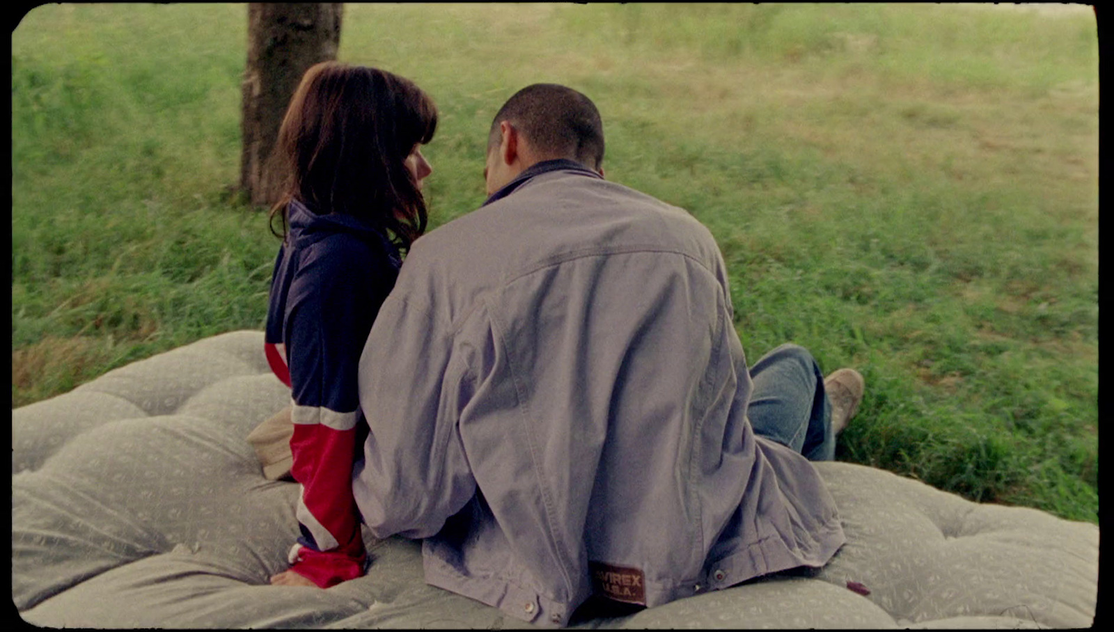 a man and a woman sitting on a mattress in a field