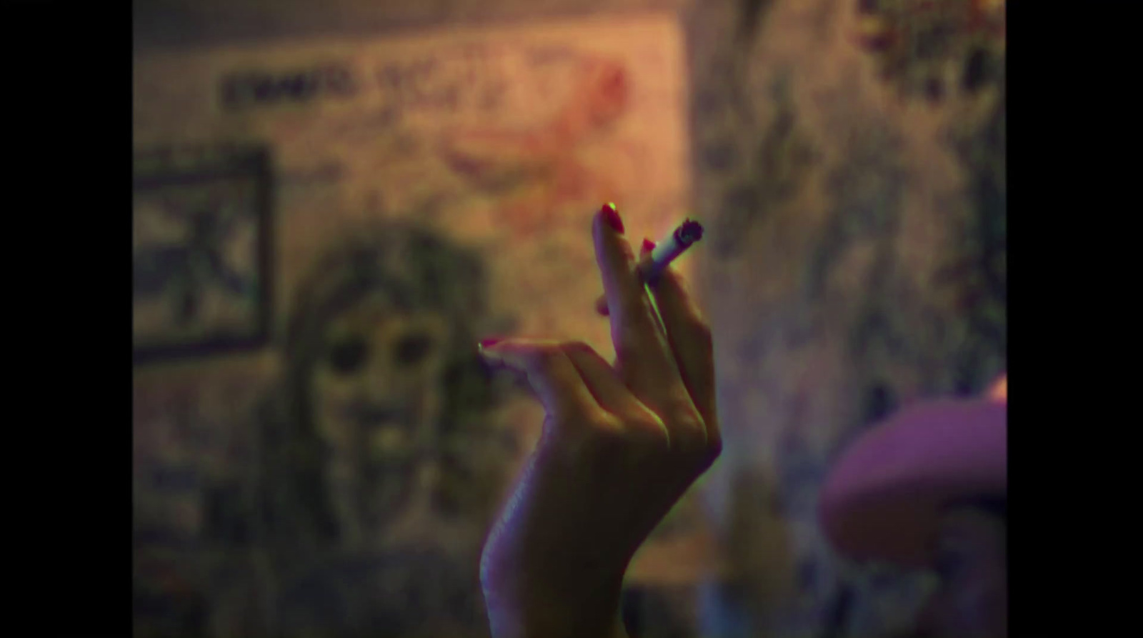 a woman's hand holding a cigarette in front of a wall