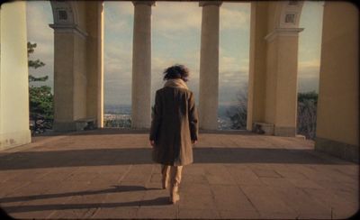 a woman walking down a walkway in front of columns