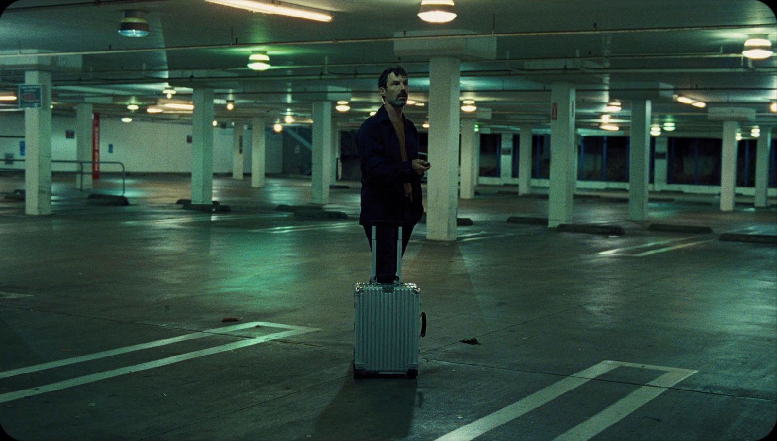 a man standing on top of a suitcase in a parking garage