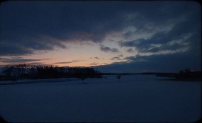 a snowy field with trees and a sky in the background