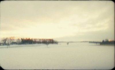 a snowy field with trees and a bridge in the distance