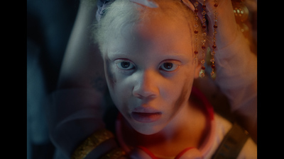 a little girl with white hair wearing a red necklace