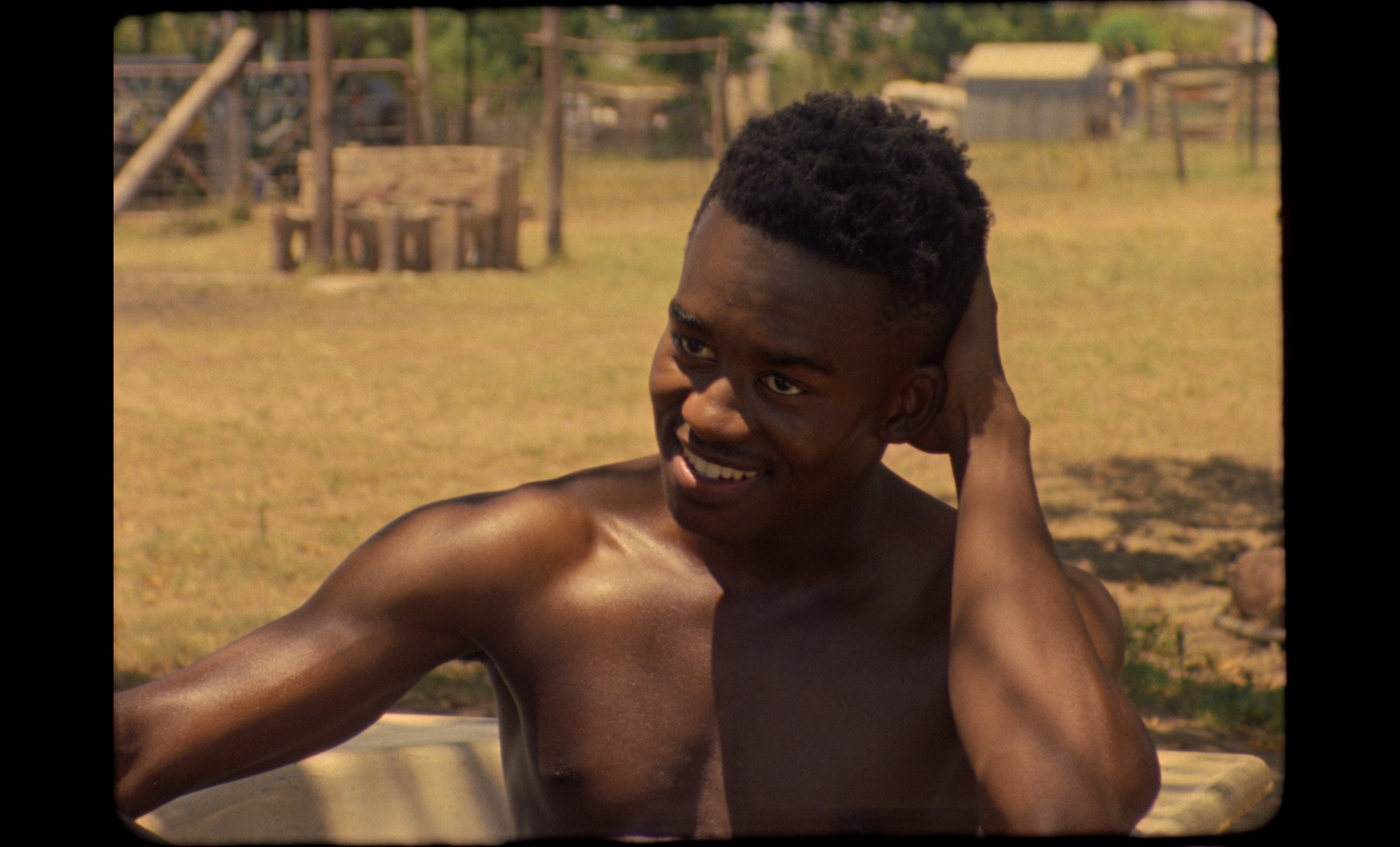 a shirtless man sitting on a bench talking on a cell phone