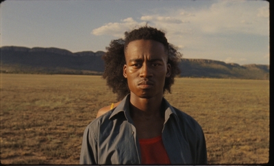 a man standing in a field with mountains in the background