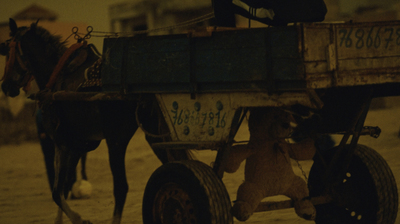 a teddy bear sitting on the back of a horse drawn carriage