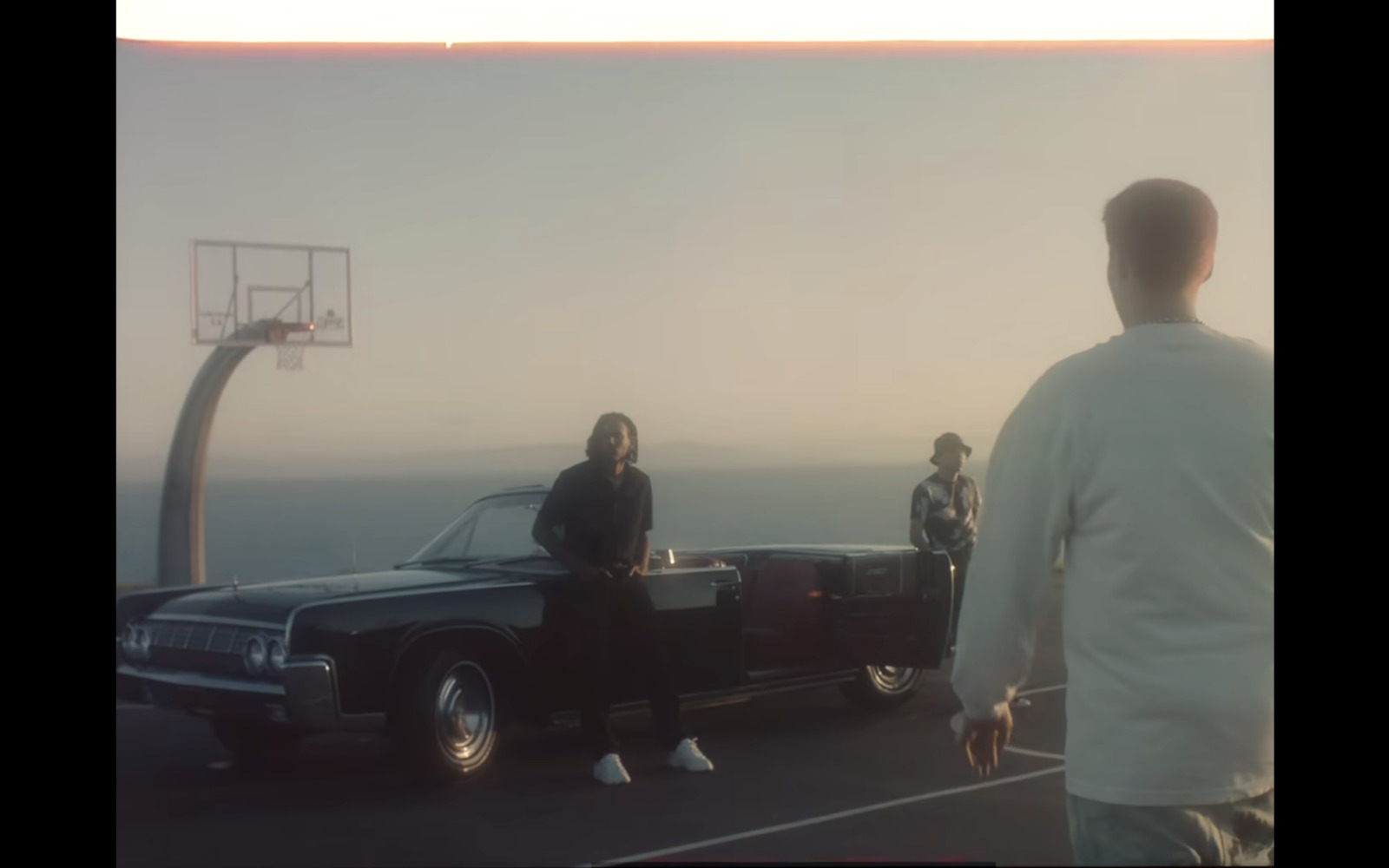 a man standing next to a black car near a basketball hoop