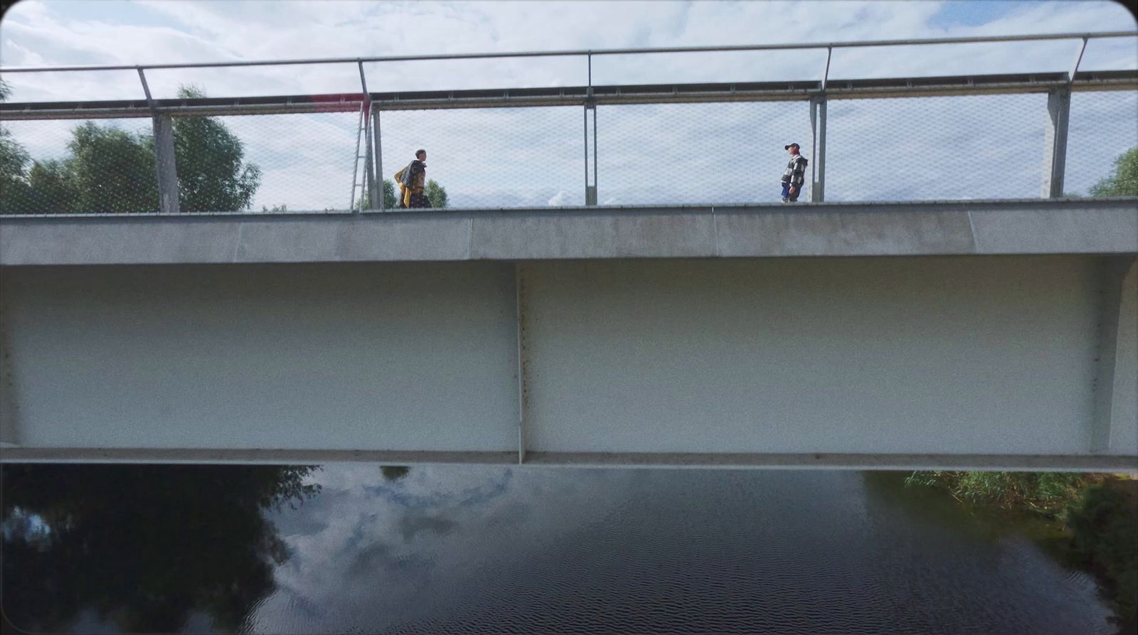 two people standing on a bridge over a body of water