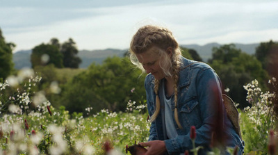 a woman standing in a field of flowers looking at her cell phone