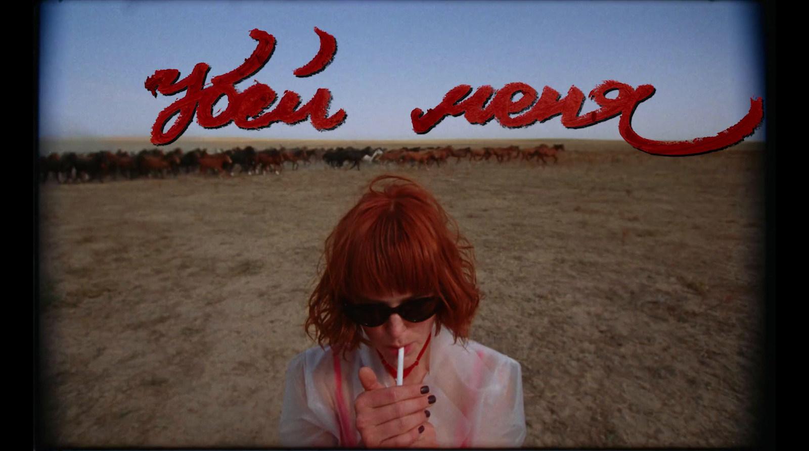 a woman holding a cigarette in front of a picture of a herd of cattle