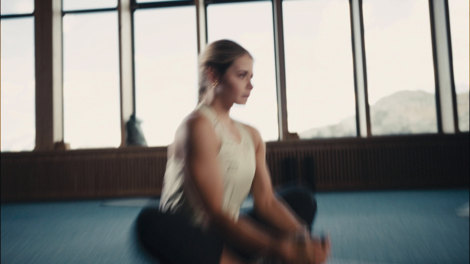 a woman squatting on a blue floor in front of large windows