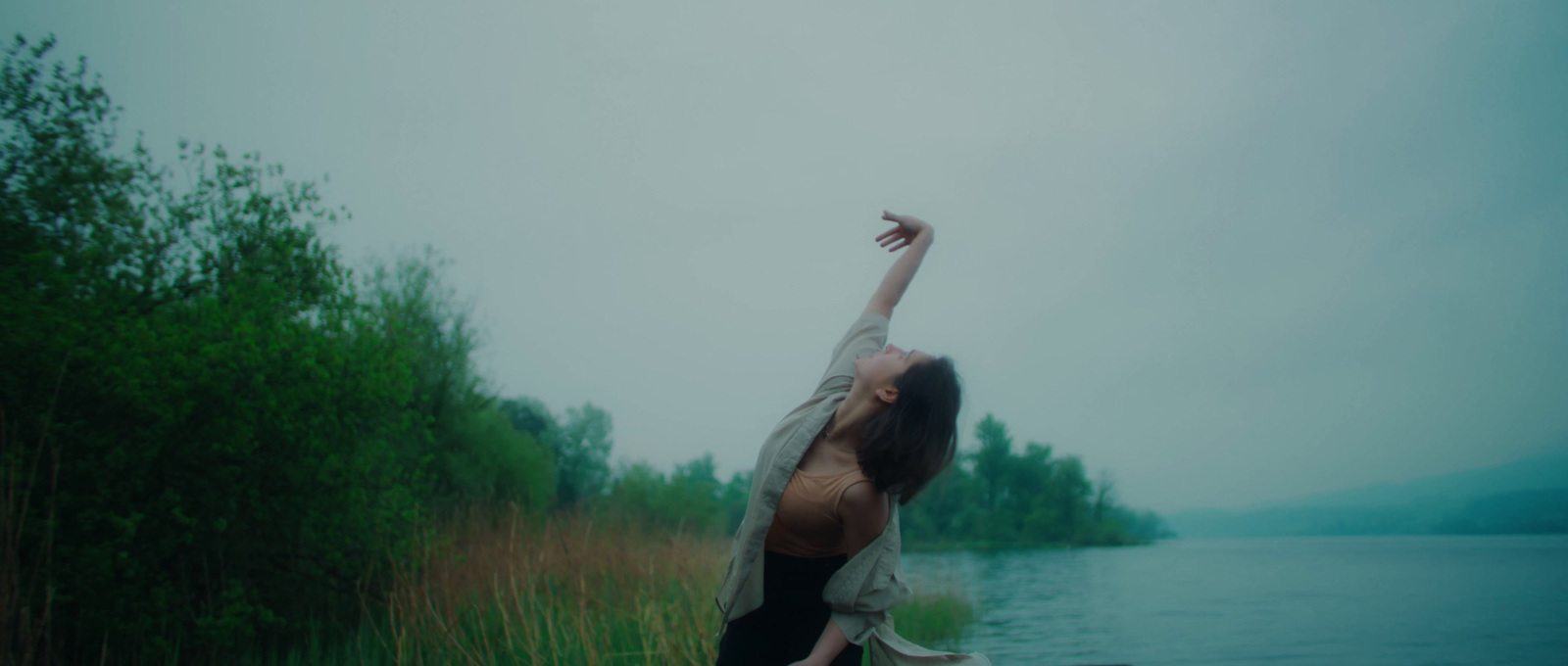 a woman reaching up into the air near a body of water