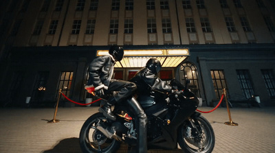 two people sitting on a motorcycle in front of a building