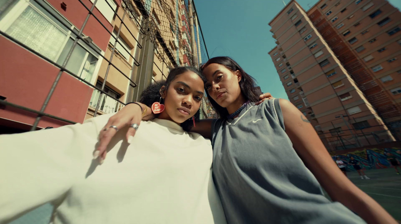 two women standing next to each other in front of tall buildings