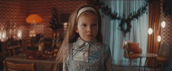 a young girl standing in a living room next to a table