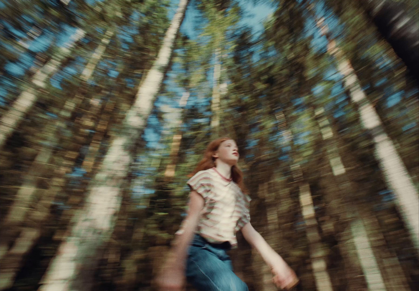 a woman is walking through the woods with a skateboard