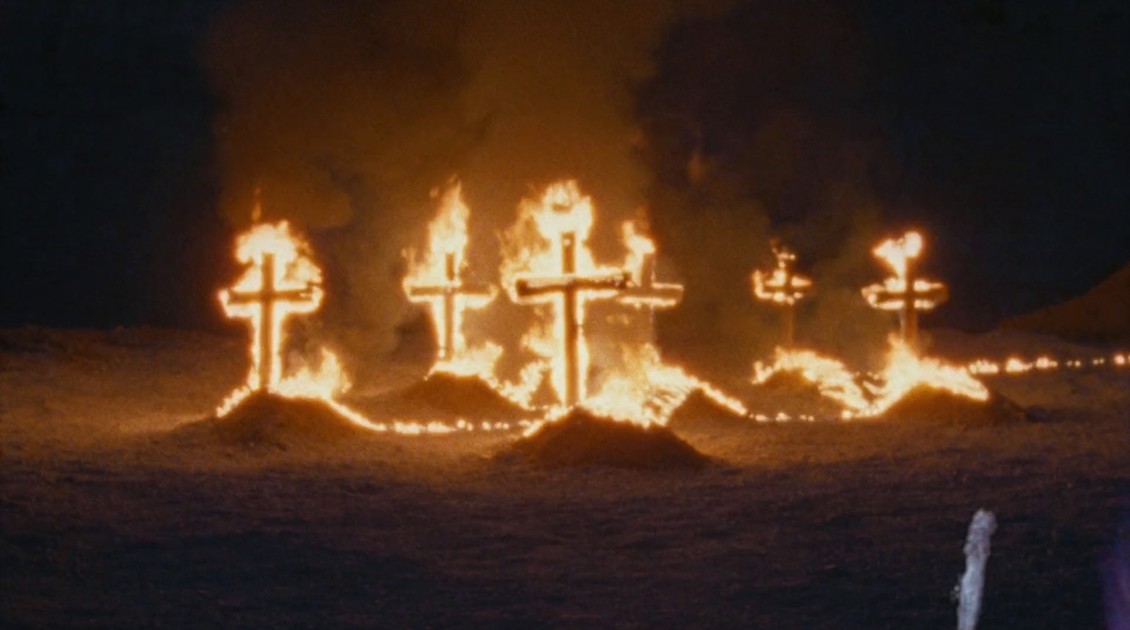 a group of people standing in front of a cross on fire