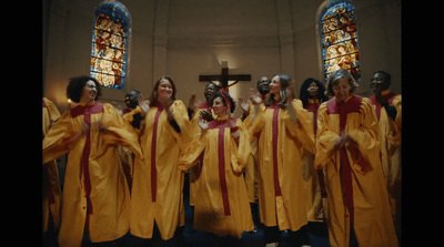 a group of women in yellow robes singing in front of a stained glass window