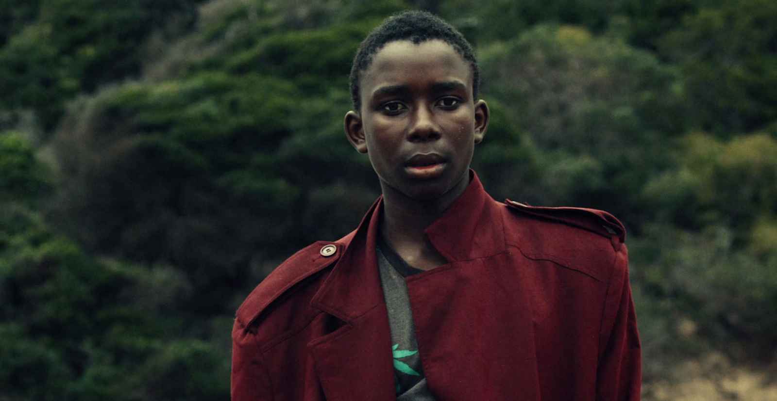 a man in a red jacket standing in front of a forest