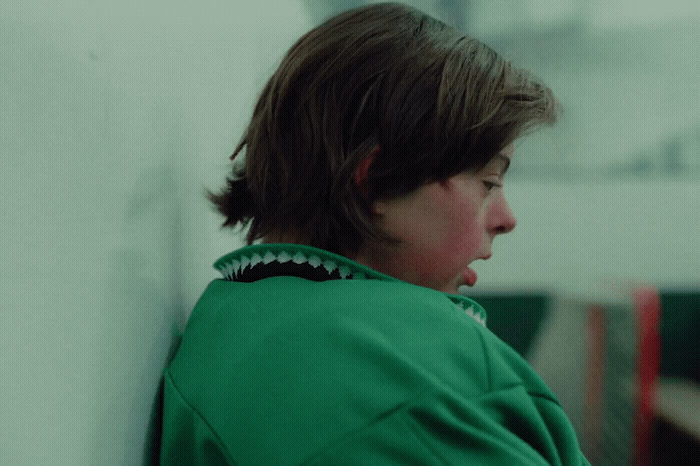 a boy in a green jacket leaning against a wall