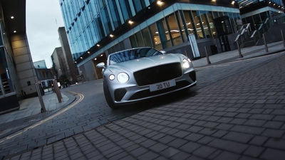 a silver car driving down a street next to tall buildings