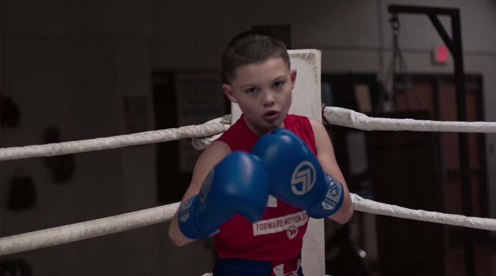 a young boy in a red shirt and blue boxing gloves