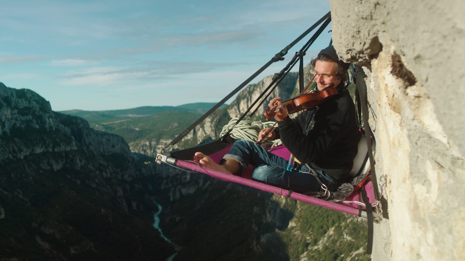 a man playing a violin while sitting in a hammock