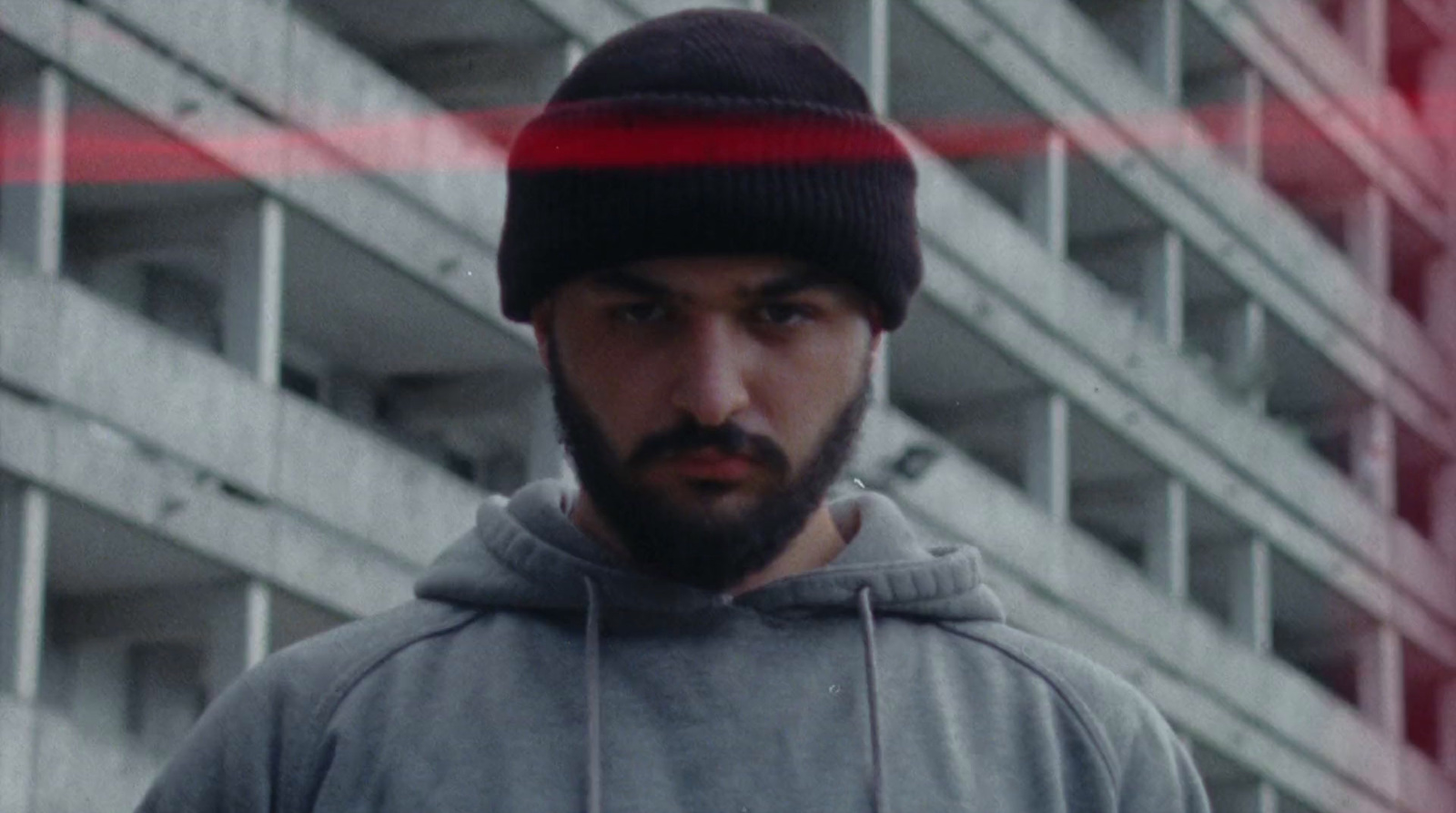 a man with a beard and a beanie standing in front of a building