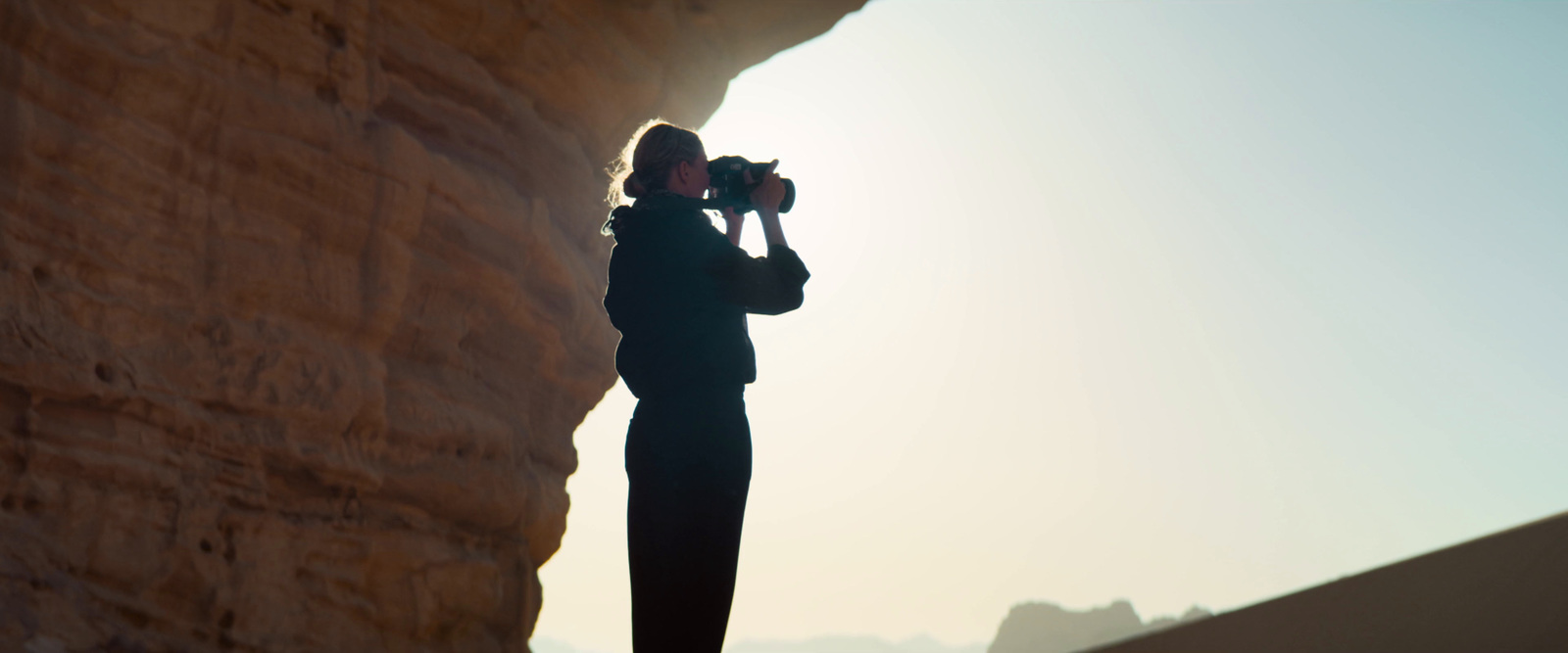 a woman standing next to a cliff with a camera