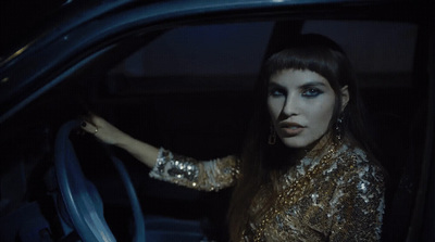 a woman sitting in a car with her hand on the steering wheel