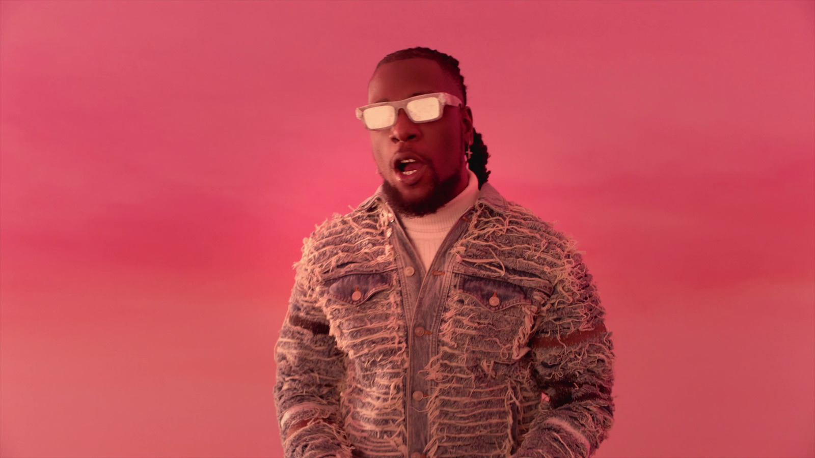 a man in a jacket and sunglasses standing in front of a pink background