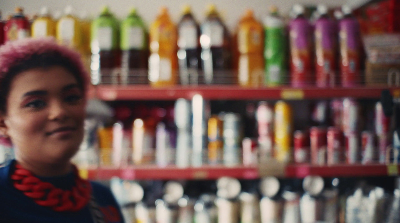 a woman with pink hair standing in front of a shelf of bottles