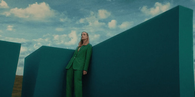 a woman in a green suit leaning against a wall