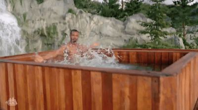 a man sitting in a wooden hot tub next to a waterfall