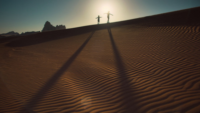 a couple of people standing on top of a sandy hill