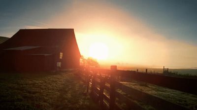 the sun is setting behind a barn on a farm