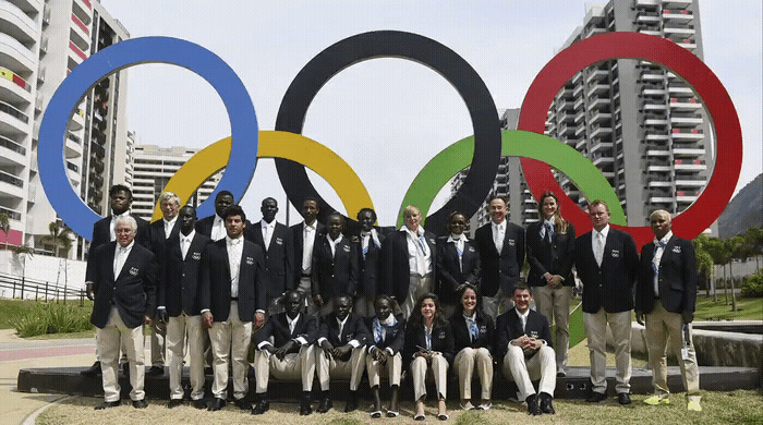 a group of men standing next to each other in front of a large olympic sign