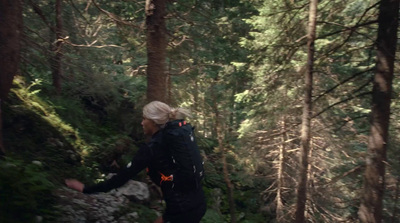 a woman walking through a forest with lots of trees