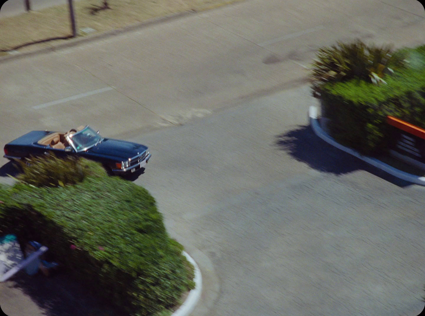 a blue car driving down a street next to a lush green bush