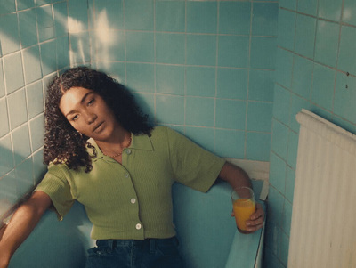 a woman in a green shirt leaning against a blue wall