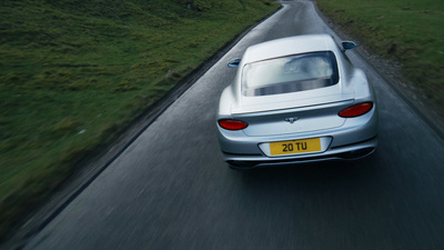 a silver car driving down a road next to a lush green hillside